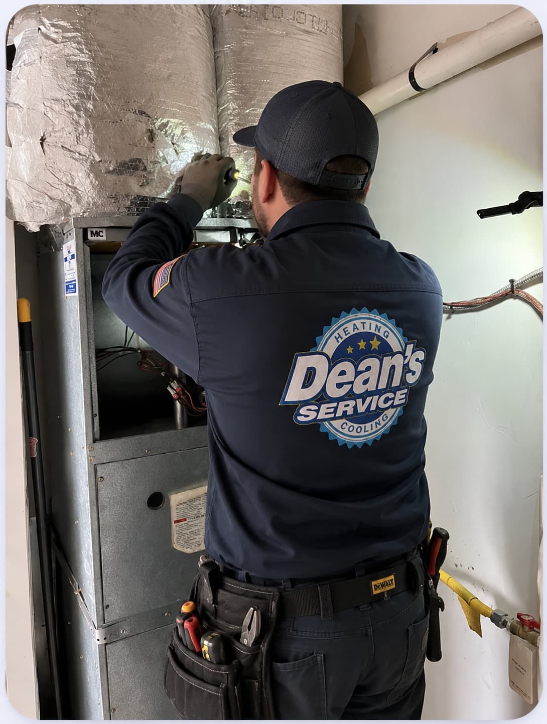 A Dean's Service technician in branded uniform servicing a home furnace and ductwork